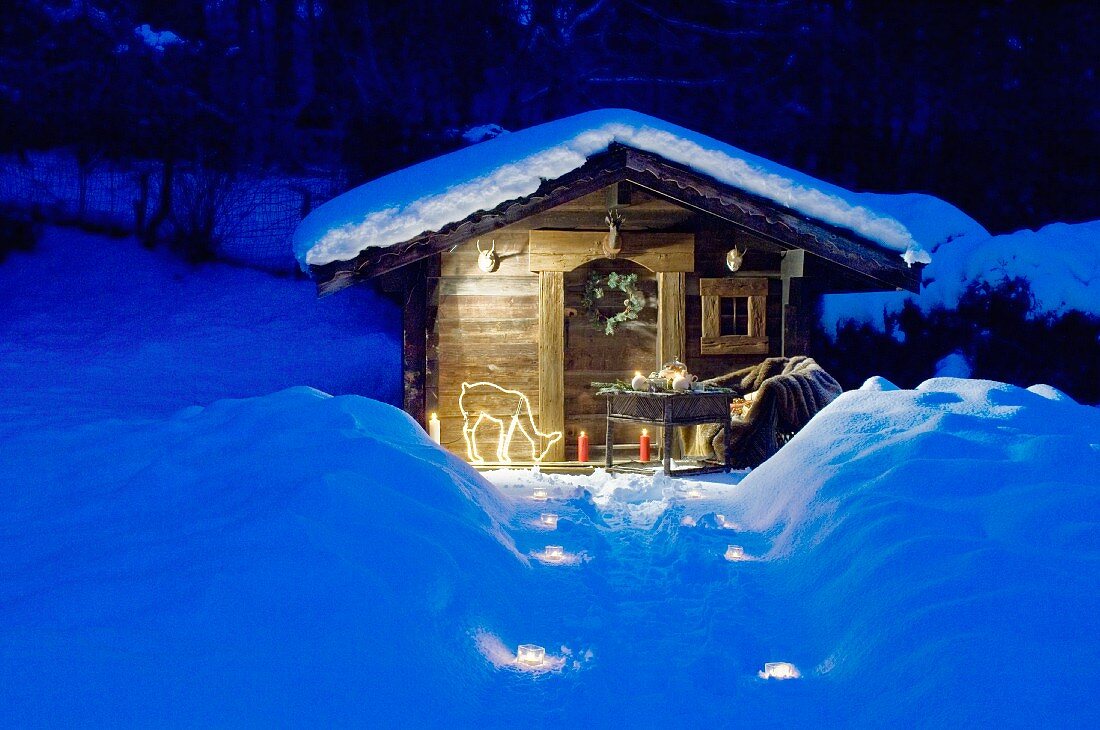 Beleuchteter Weg zur verschneiten Gartenhütte im Alpenstil