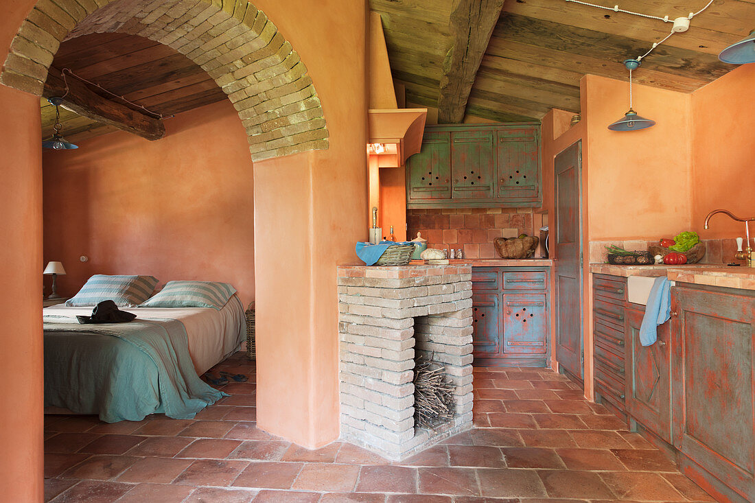 Mediterrane Küche mit Terrakottafliesen und Kamin, Blick durch Rundbogenöffnung ins Schlafzimmer