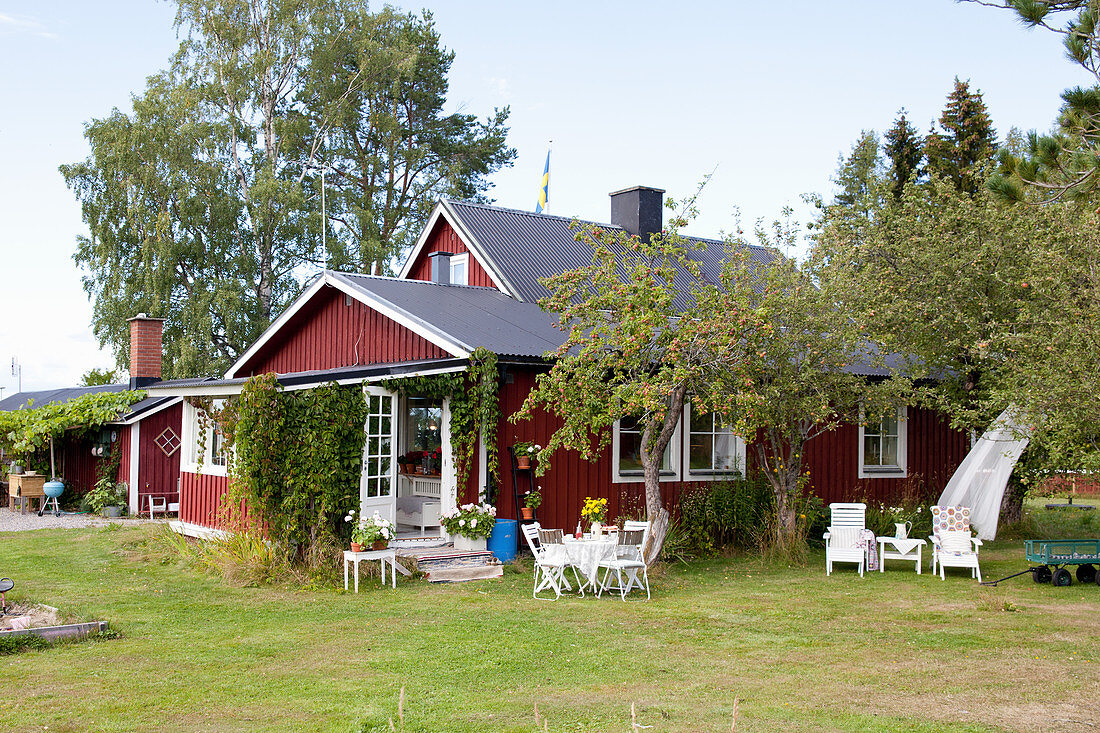 Rotes Schwedenhaus mit Sitzplätzen im sommerlichen Garten