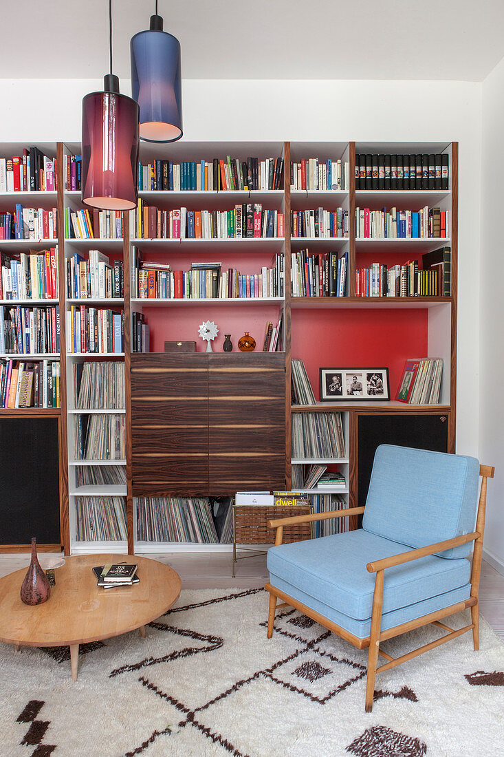 Retrosessel und runder Couchtisch vor Bücherregal mit roter Rückwand