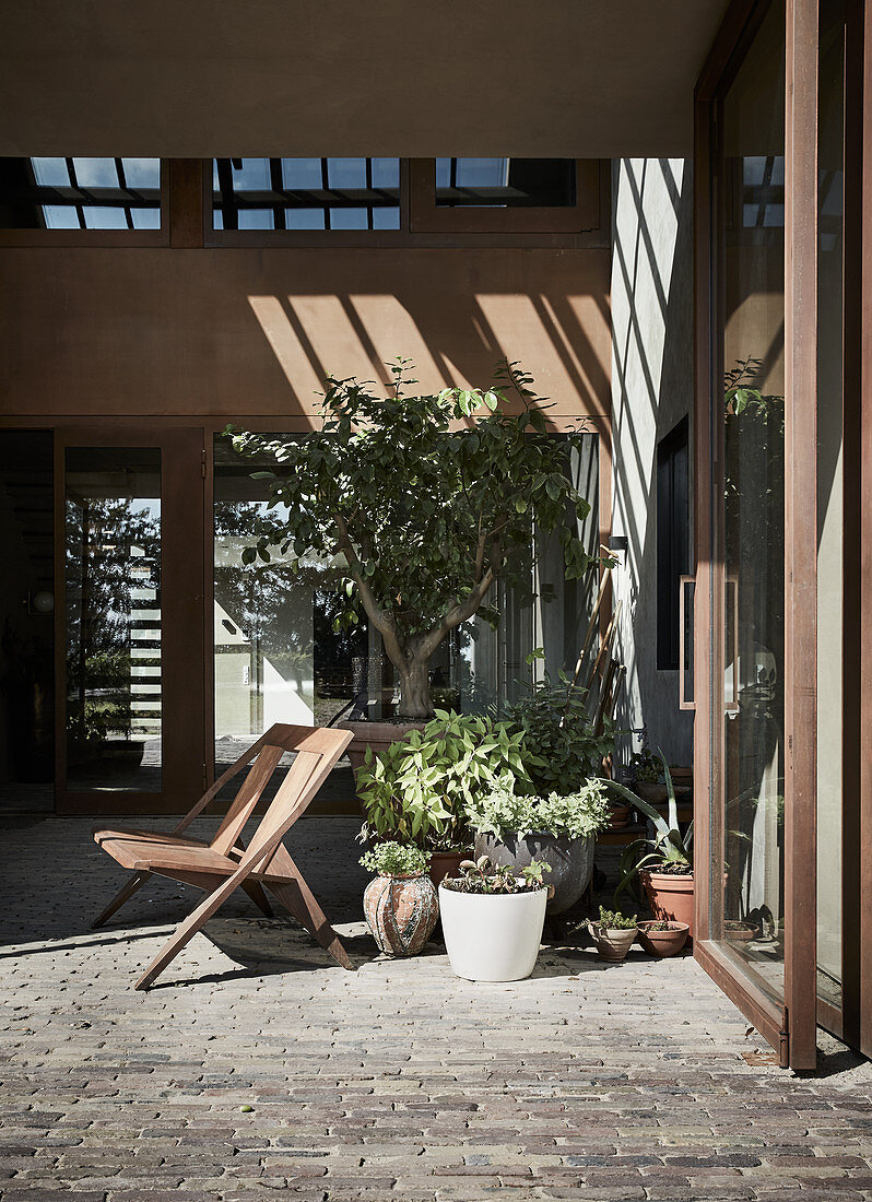 Stuhl und Topfpflanzen auf Terrasse mit Kopfsteinpflastern