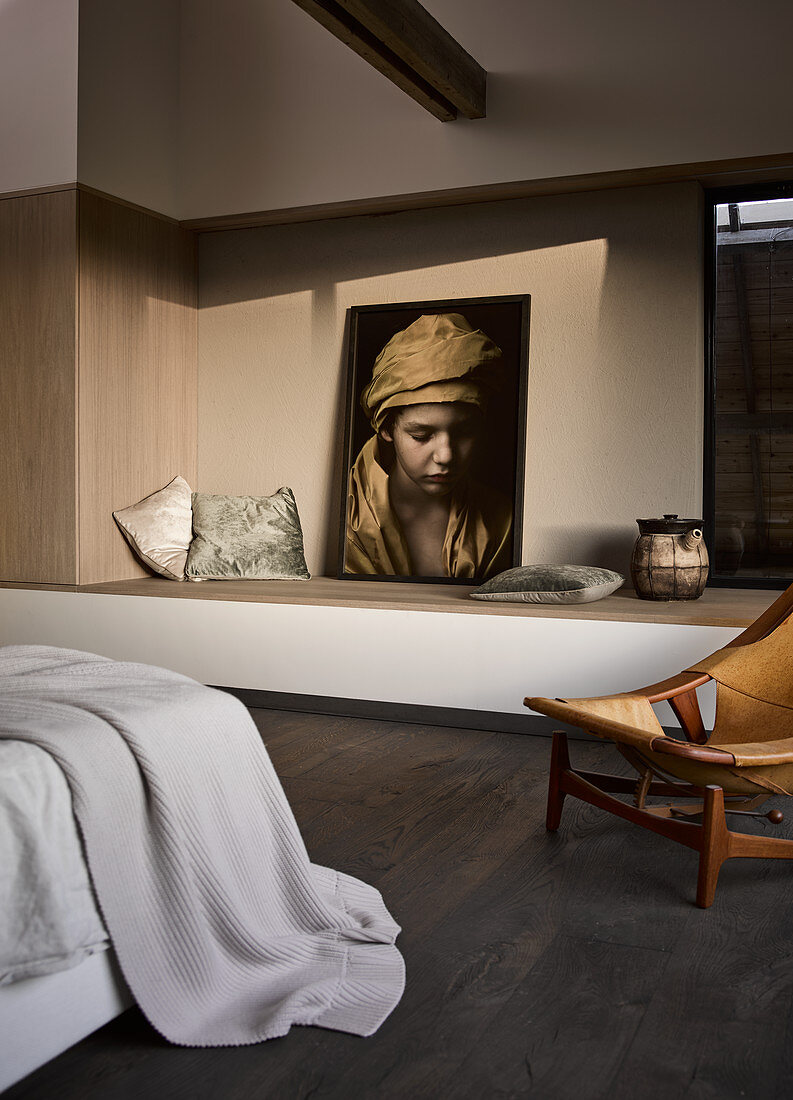 Large photo on masonry ledge and vintage chair in bedroom with dark wooden floor