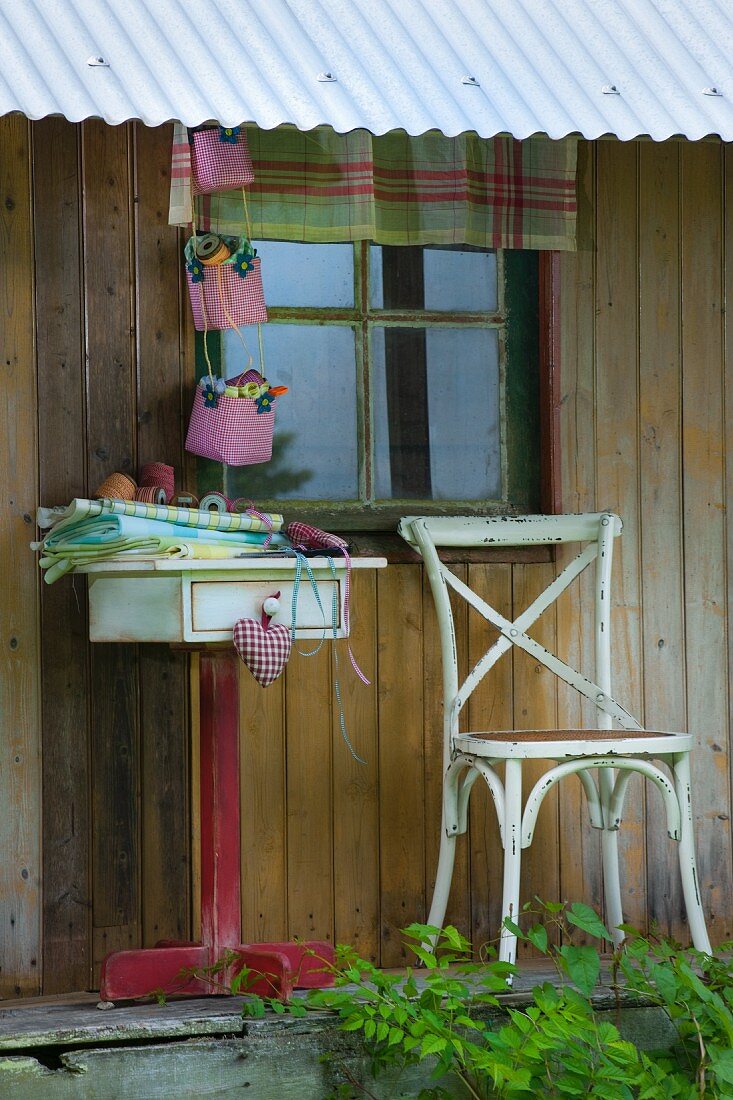 Hand-sewn fabric containers above folded fabrics on small table against rustic wooden façade
