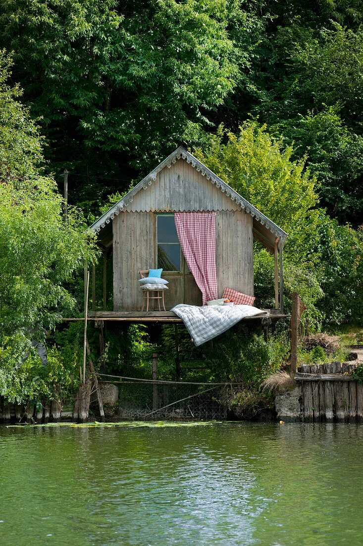 Romantic sleeping area on wooden terrace of rustic fisherman's hut next to lake