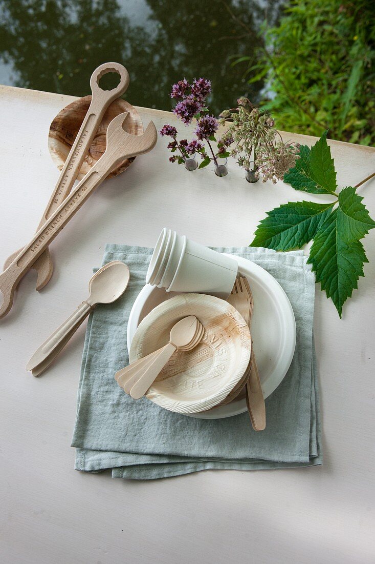 Various wooden cutlery, paper cups and bowls arranged on linen napkin
