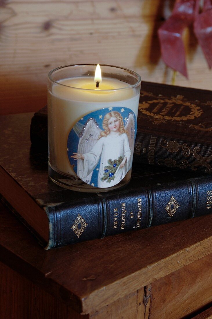 Lit candle in jar with angel motif on top of antique book