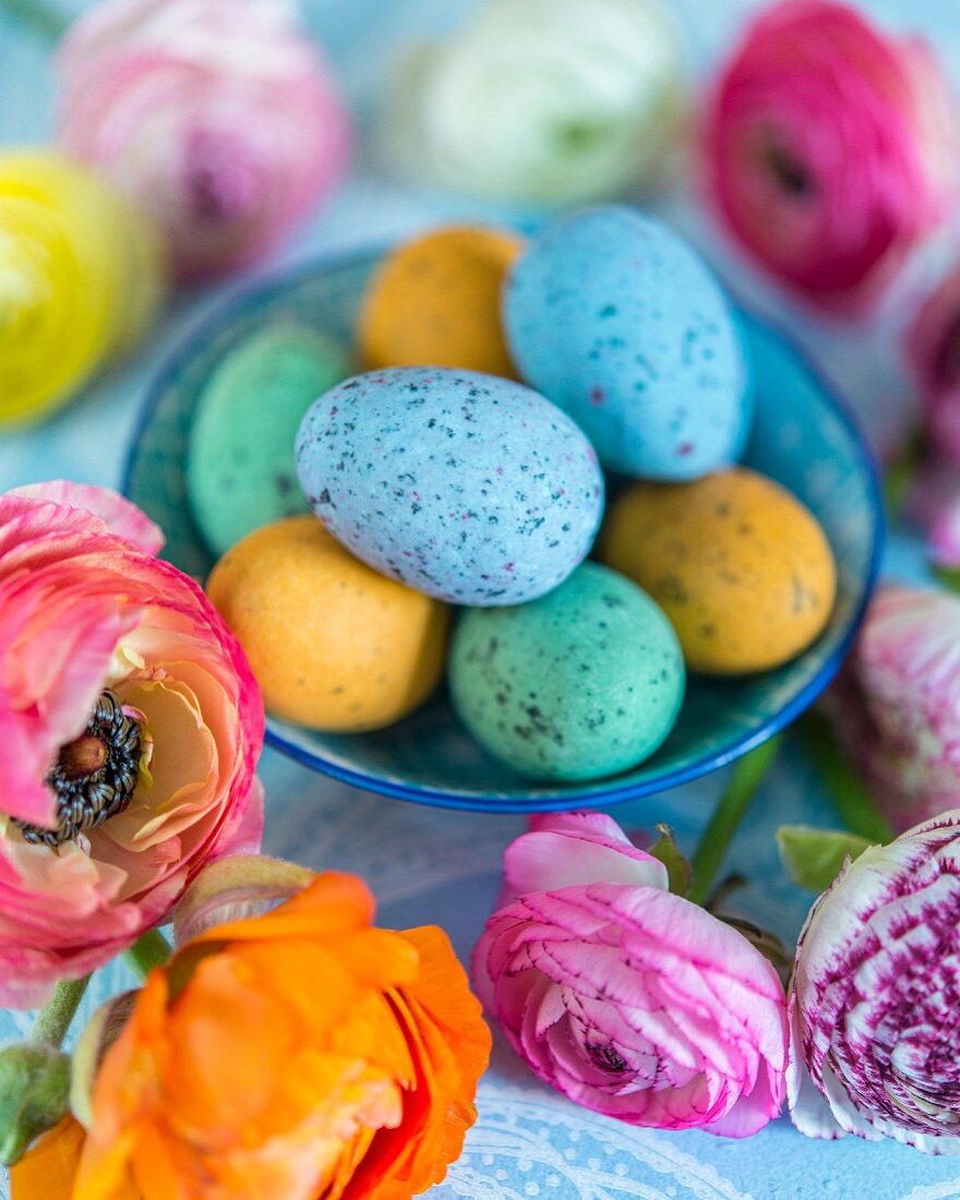 Colourful speckled eggs in bowls amongst ranunculus flowers