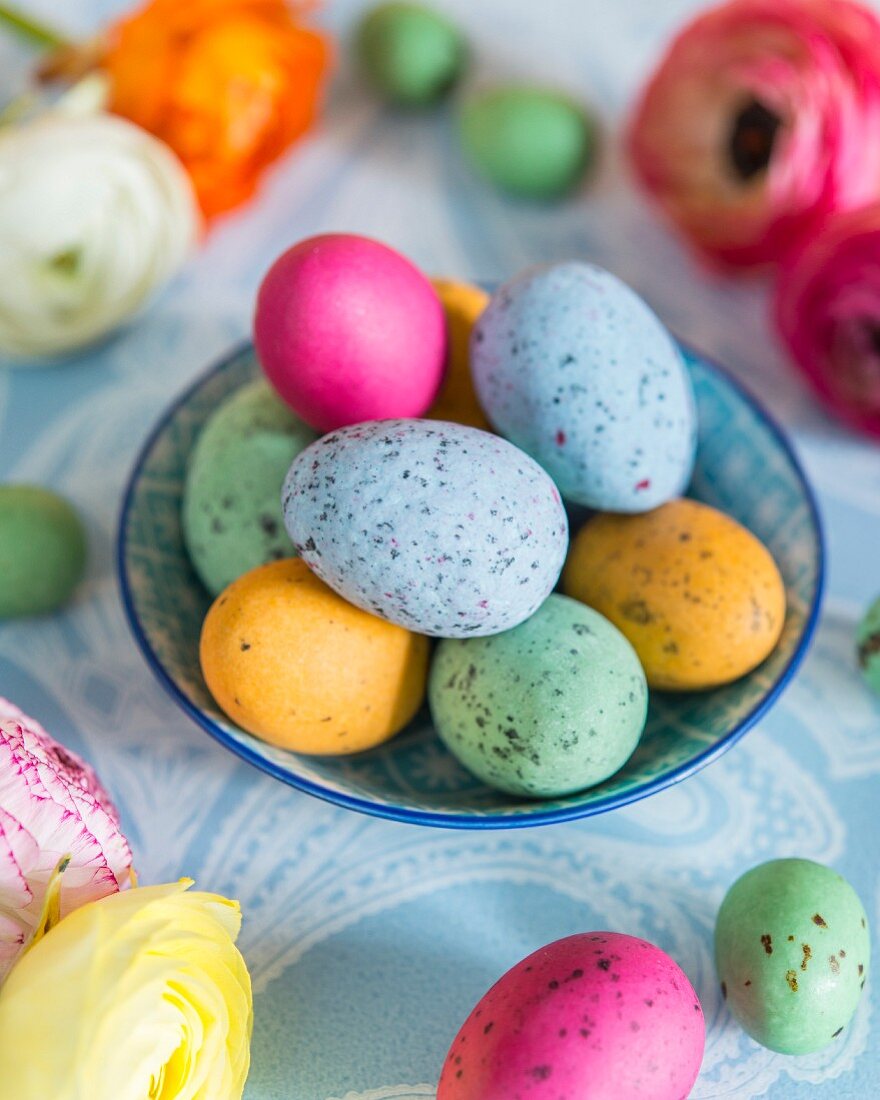 Colourful speckled eggs in bowl; Easter arrangement on pale blue tablecloth