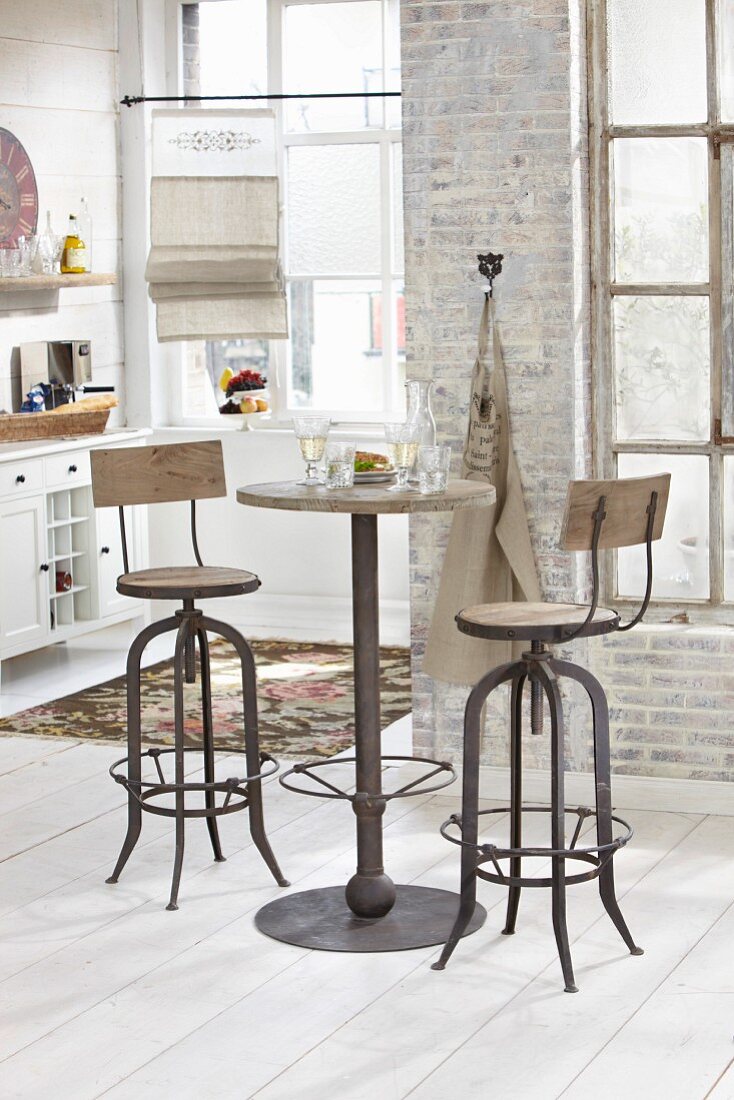 High, vintage table and two bar stools in front of brick wall in period apartment