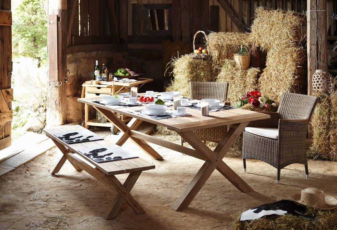 Set dining table, serving trolley and bales of straw in rustic barn