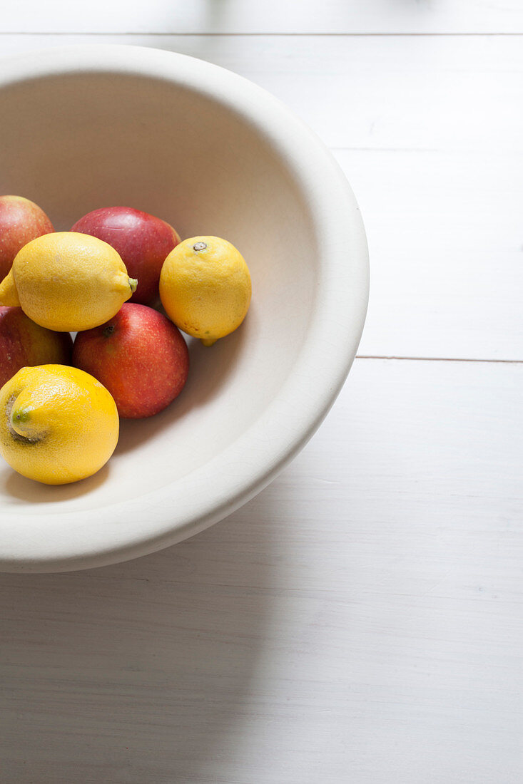 Lemons and apples in white fruit bowl on white table