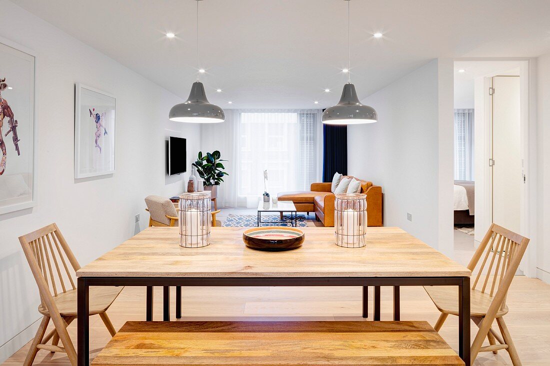 Dining table with metal frame and wooden top, wooden bench and wooden chairs in open-plan interior