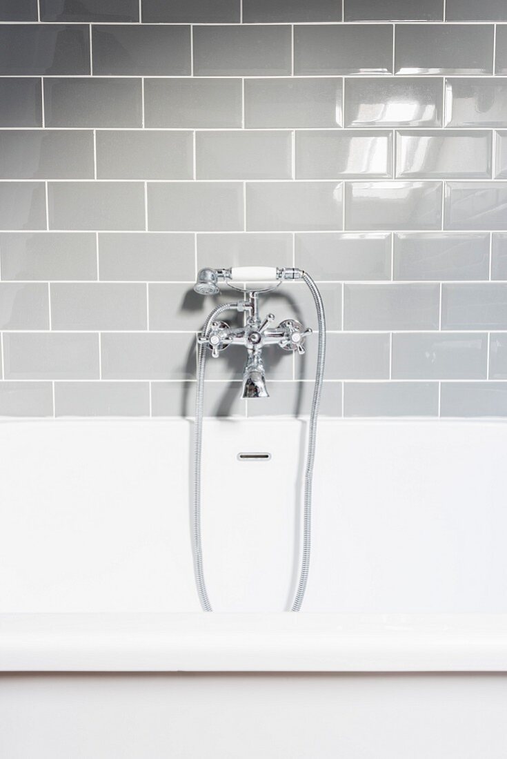 Vintage tap fittings on bathtub below grey wall tiles