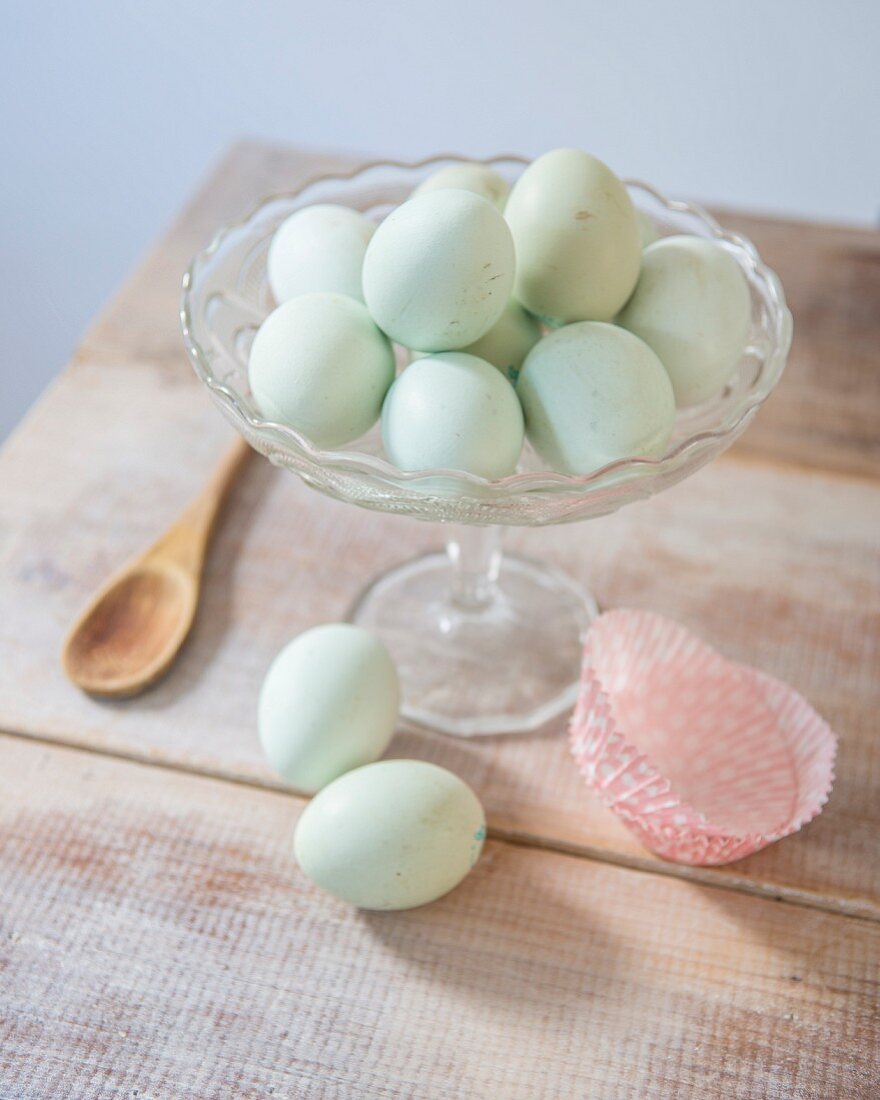 Mintgrün gefärbte Eier in Glasschale und auf rustikalem Holztisch