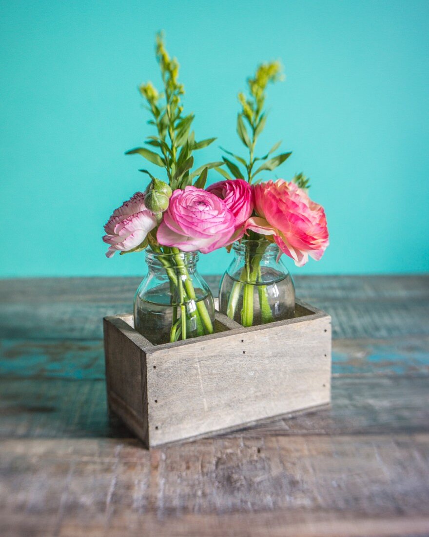 Ranunculus in glass bottles in wooden box against turquoise background