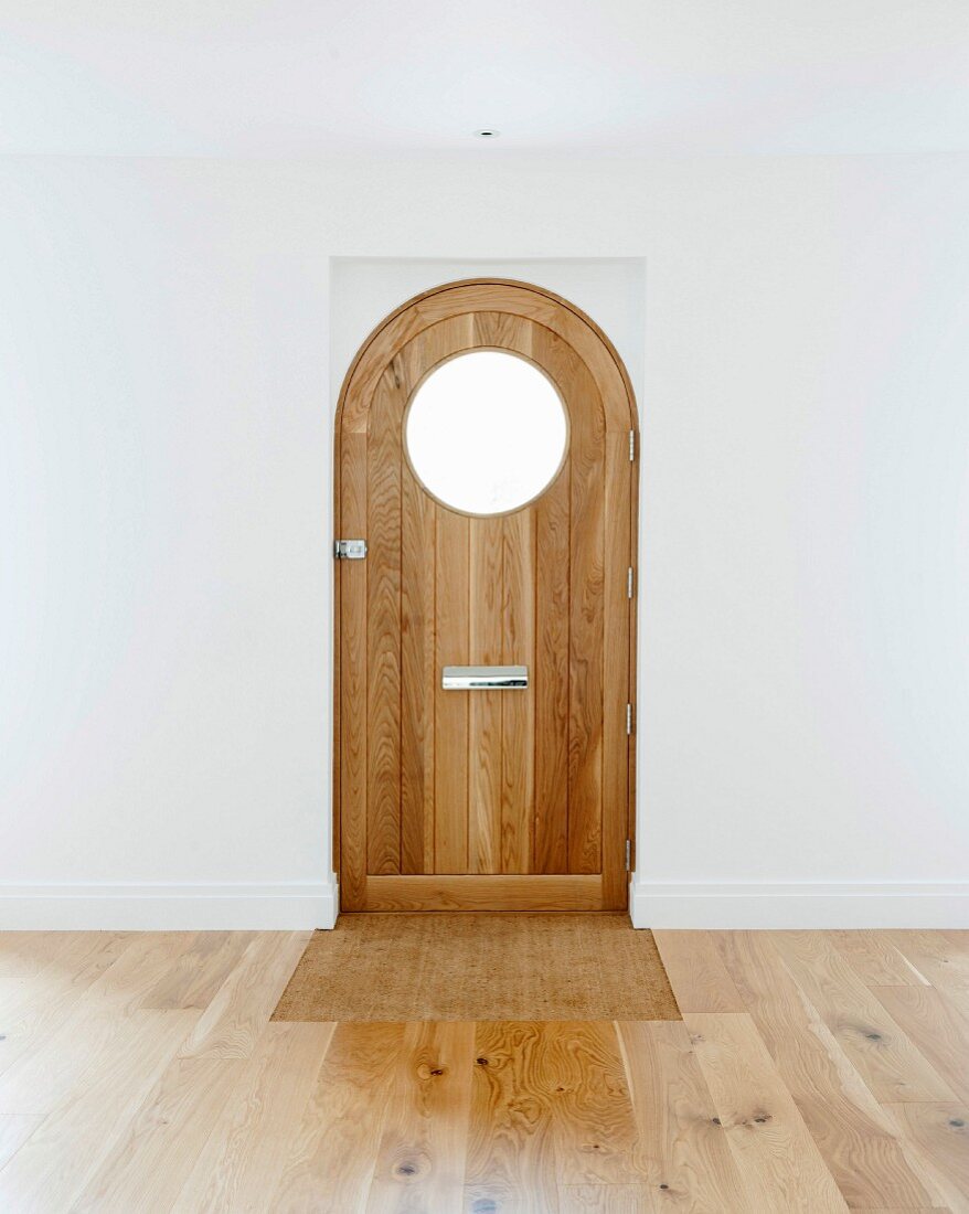 Front door with round window in empty room with oak parquet floor