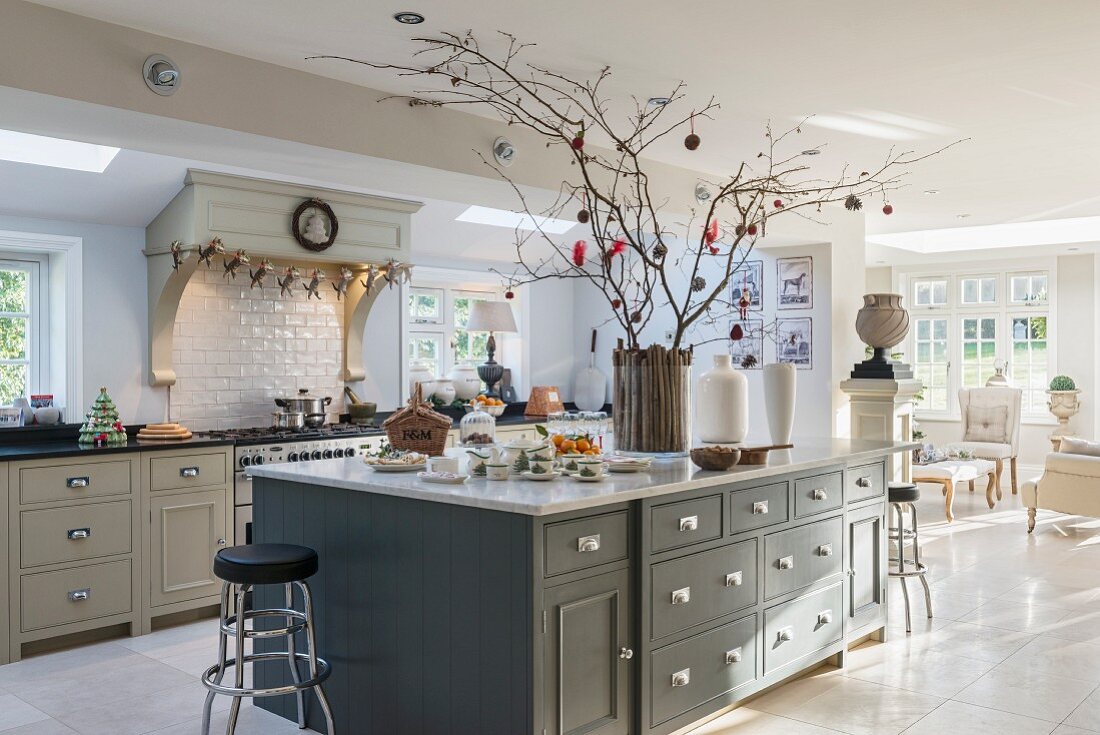 Bright, open-plan, country-house kitchen with arrangement of branches on island counter