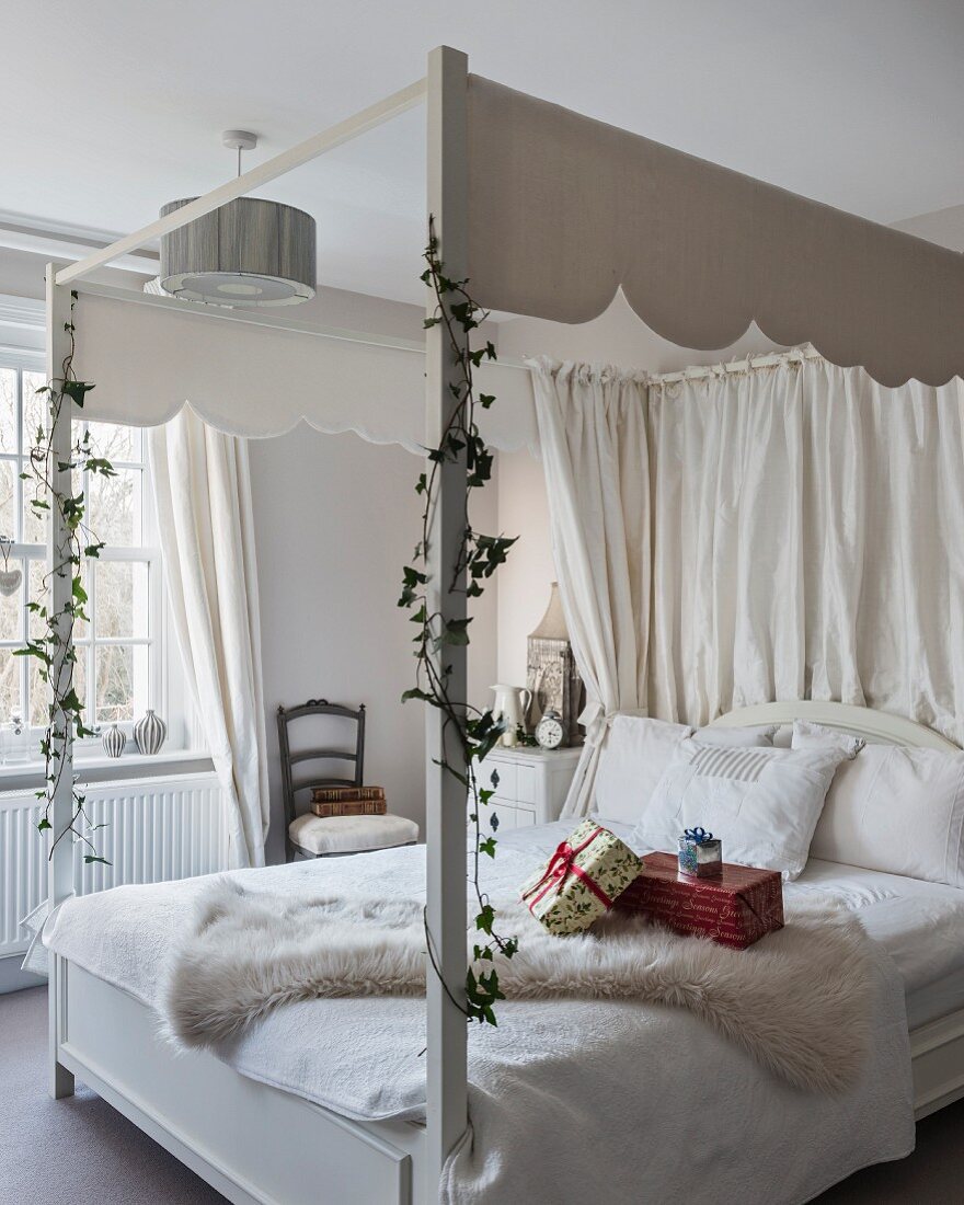 Wrapped presents on white four-poster bed with canopy decorated with ivy tendrils
