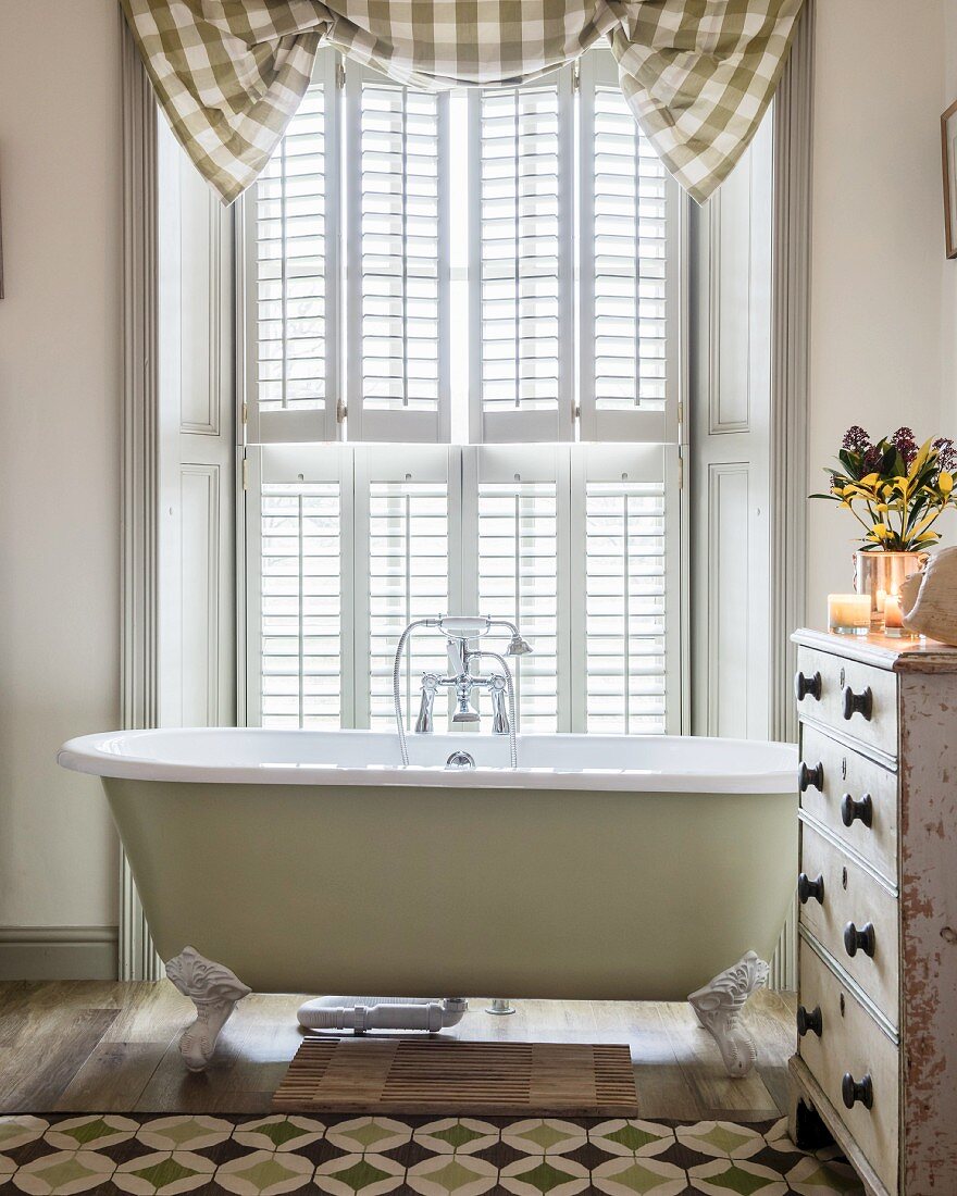 Free-standing bathtub in front of French window with shutters