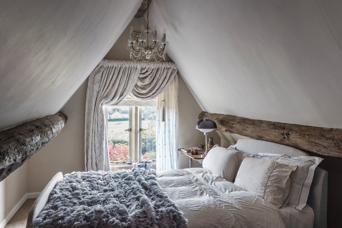 Fur blanket on bed below chandelier in attic bedroom