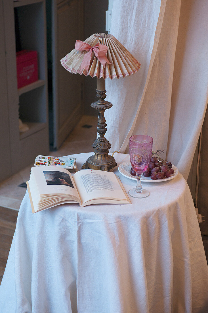 Aufgeschlagenes Buch und Leuchte auf dem Tischchen mit weißer Decke