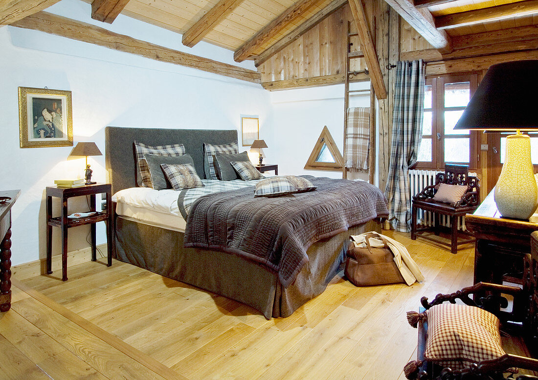 Doppelbett mit braunen und grünen Textilien in rustikalem Schlafzimmer mit Holzbalkendecke und Sprossenfenstern