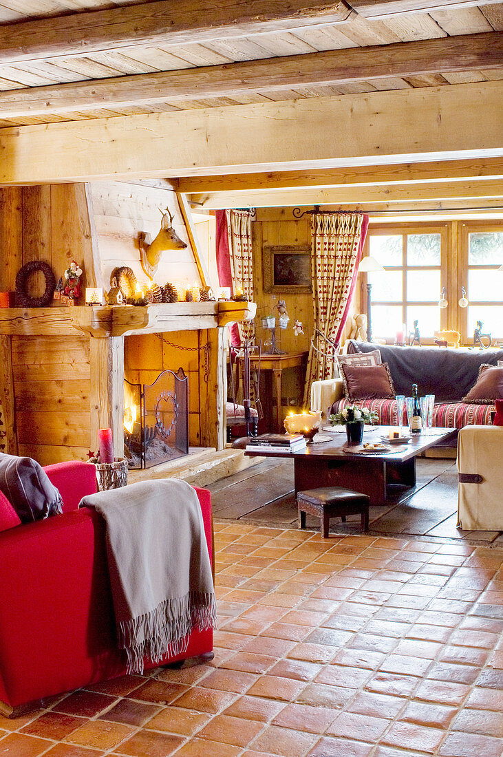 Offener Wohnraum mit rotem Sessel, Kamin mit Holzverkleidung, Polstergarnitur und Couchtisch im Chalet