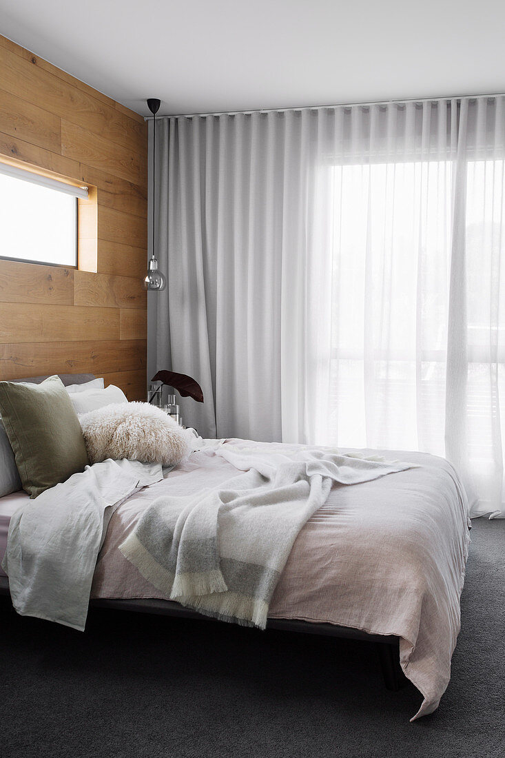 Doppelbett im Schlafzimmer mit Wand aus recyceltem Eichenholz, Fenster mit bodenlangem Vorhang