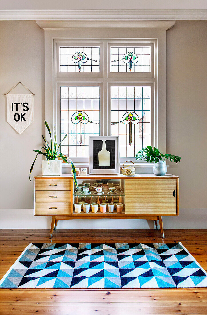 Sideboard aus hellem Holz mit Zimmerpflanzen und Teppich im geometrischen Muster