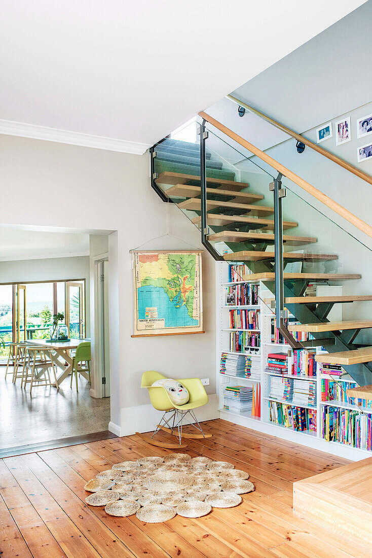 Moderne Treppenkonstruktion mit Glasgeländer und Bücherregal in einem hellen Wohnraum