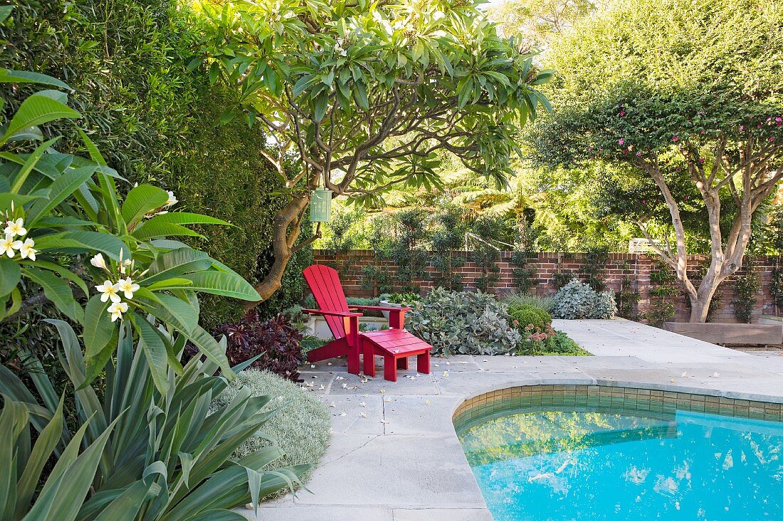 Roter Deckchair am Pool im sommerlichen Garten