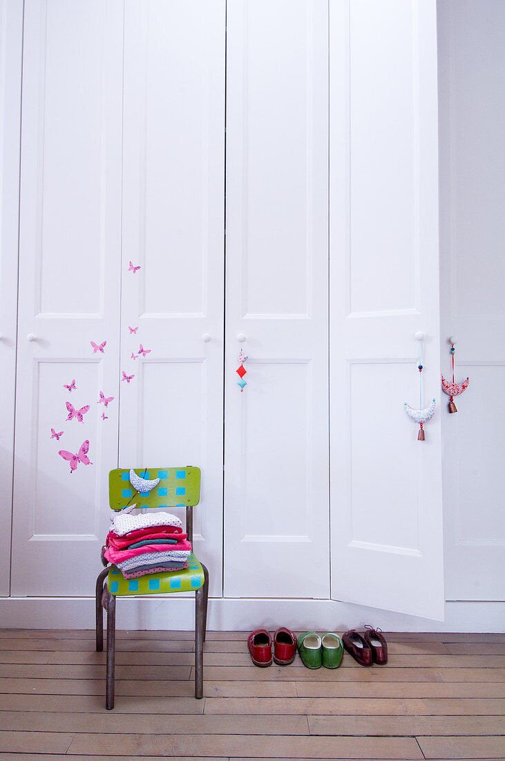 White fitted wardrobe with butterfly motifs, clothes on chair and children's shoes in room in period building