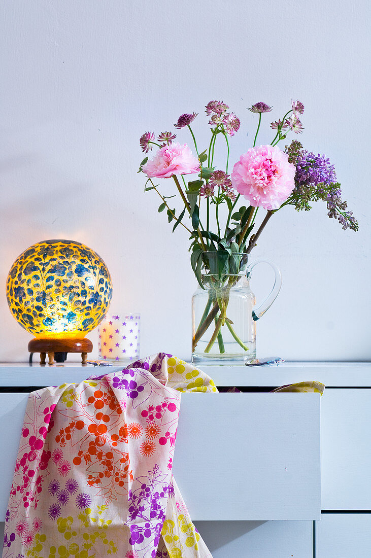 Blumenstrauß in Glaskrug und Retro Tischleuchte auf Schubladenkommode