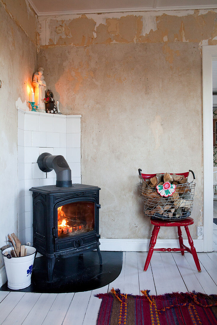 Fire in log burner in corner against stripped plaster walls