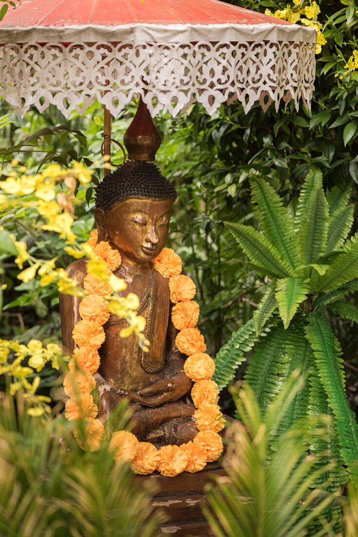 Buddhafigur mit einer Blumenkette unter balinesischem Sonnenschirm