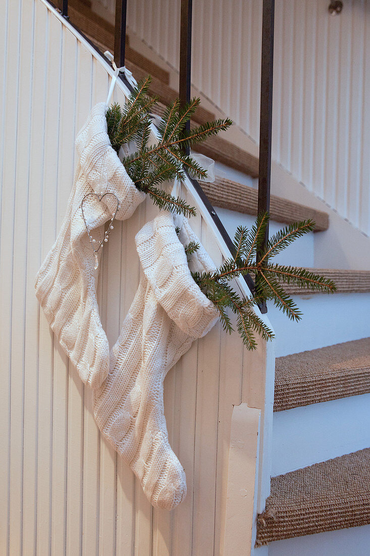Fir branches in two white knitted Christmas stockings hung from stairs
