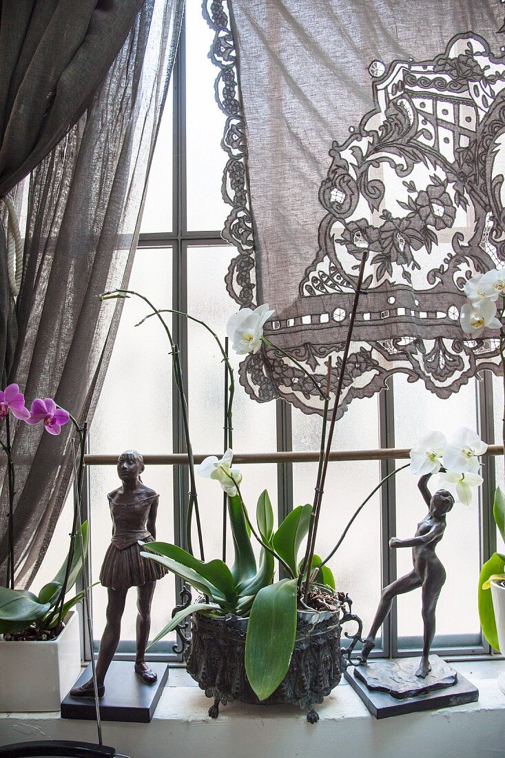 Spitzenvorhang und zwei Skulpturen mit Orchideen auf Fenstersims