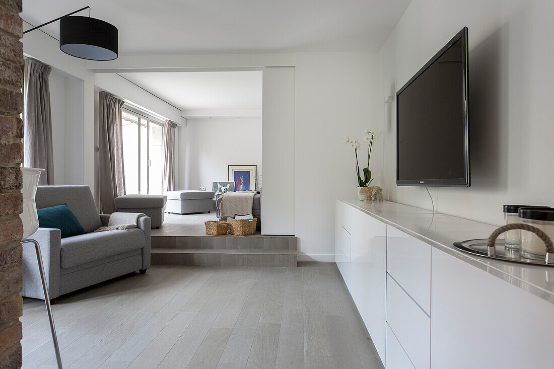 White sideboard and grey armchair in TV room with open sliding door leading into living room