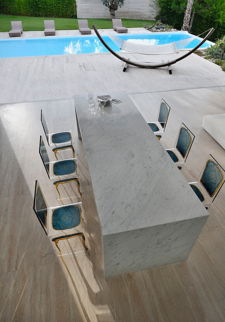 Transparente Stühle mit Barockprint am Marmortisch vor dem Pool