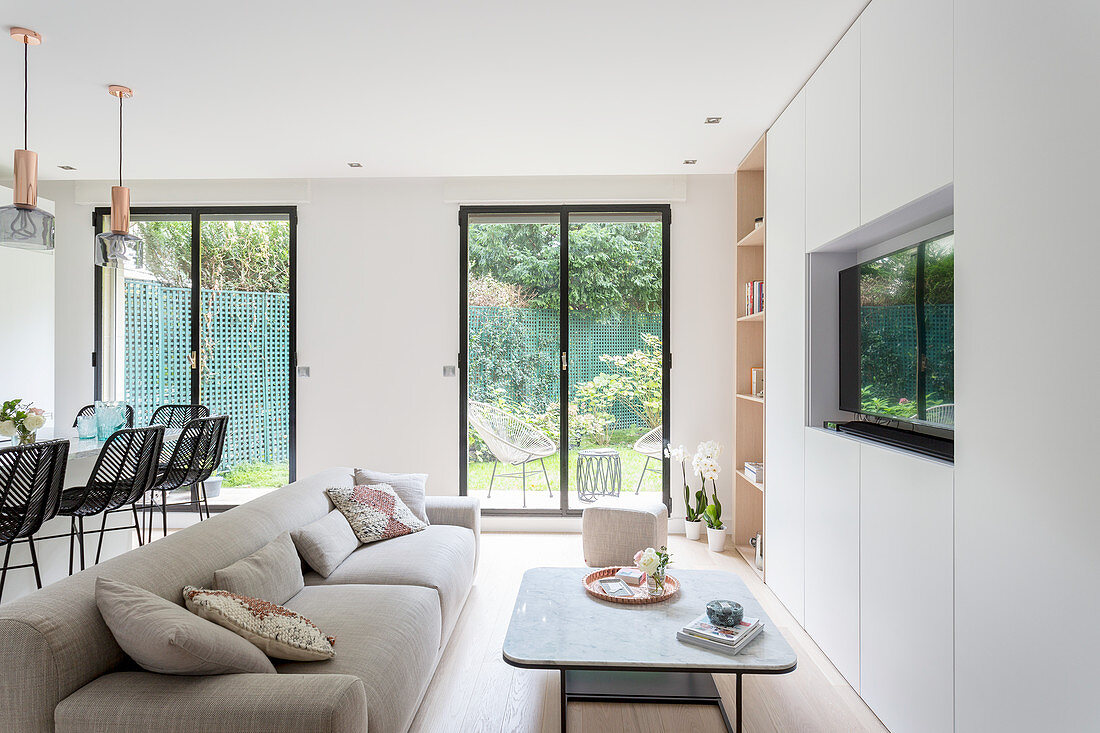 Moderne Schrankwand mit Fernseher, Couchtisch und Polstersofa im Wohnzimmer mit bodentiefen Fenstern zum Garten