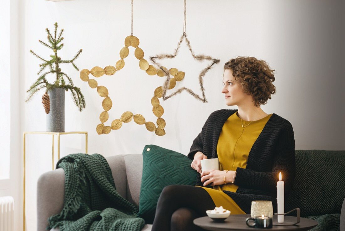 Frau sitzt auf Sofa vor DIY-Weihnachtssternen aus Naturmaterialien