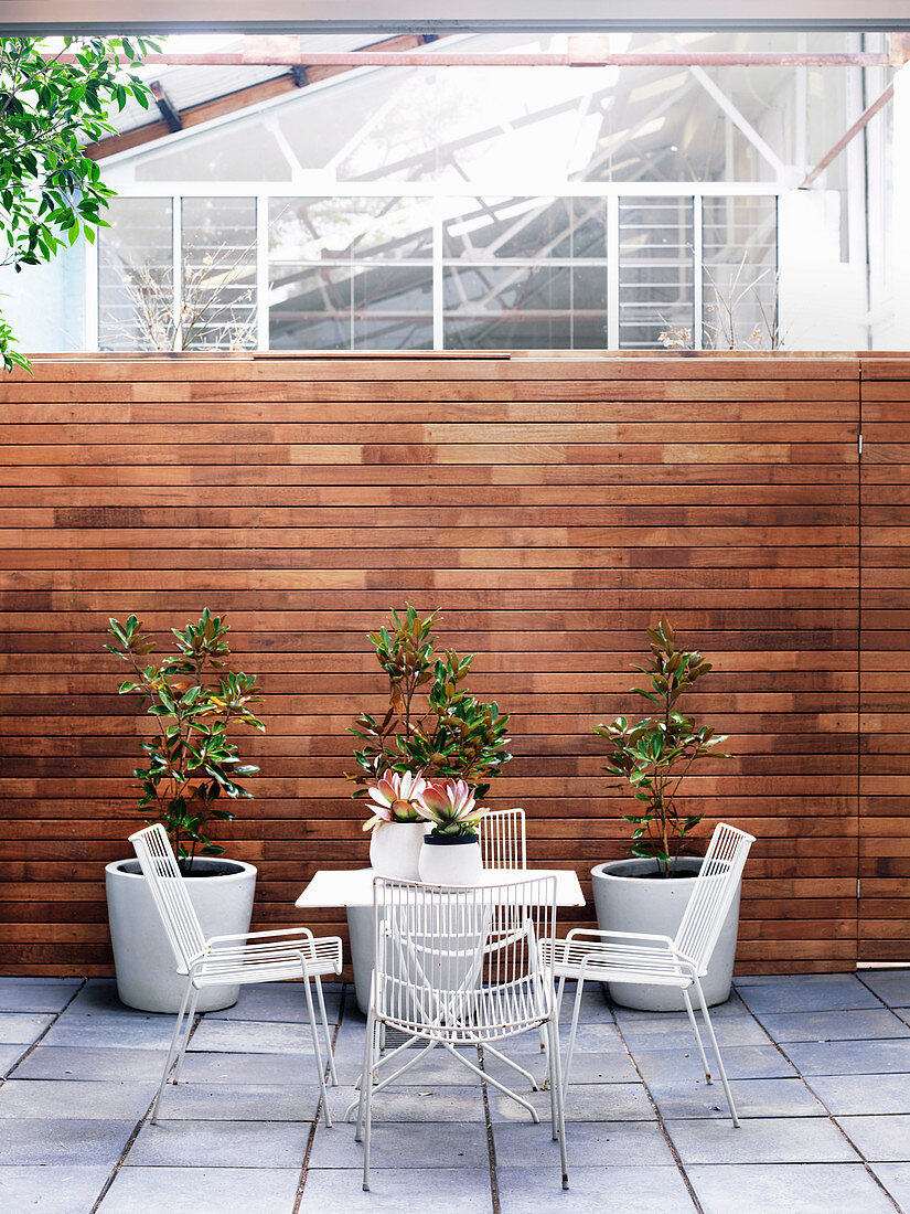 Table with chairs and plant pots in the courtyard with wooden privacy screen