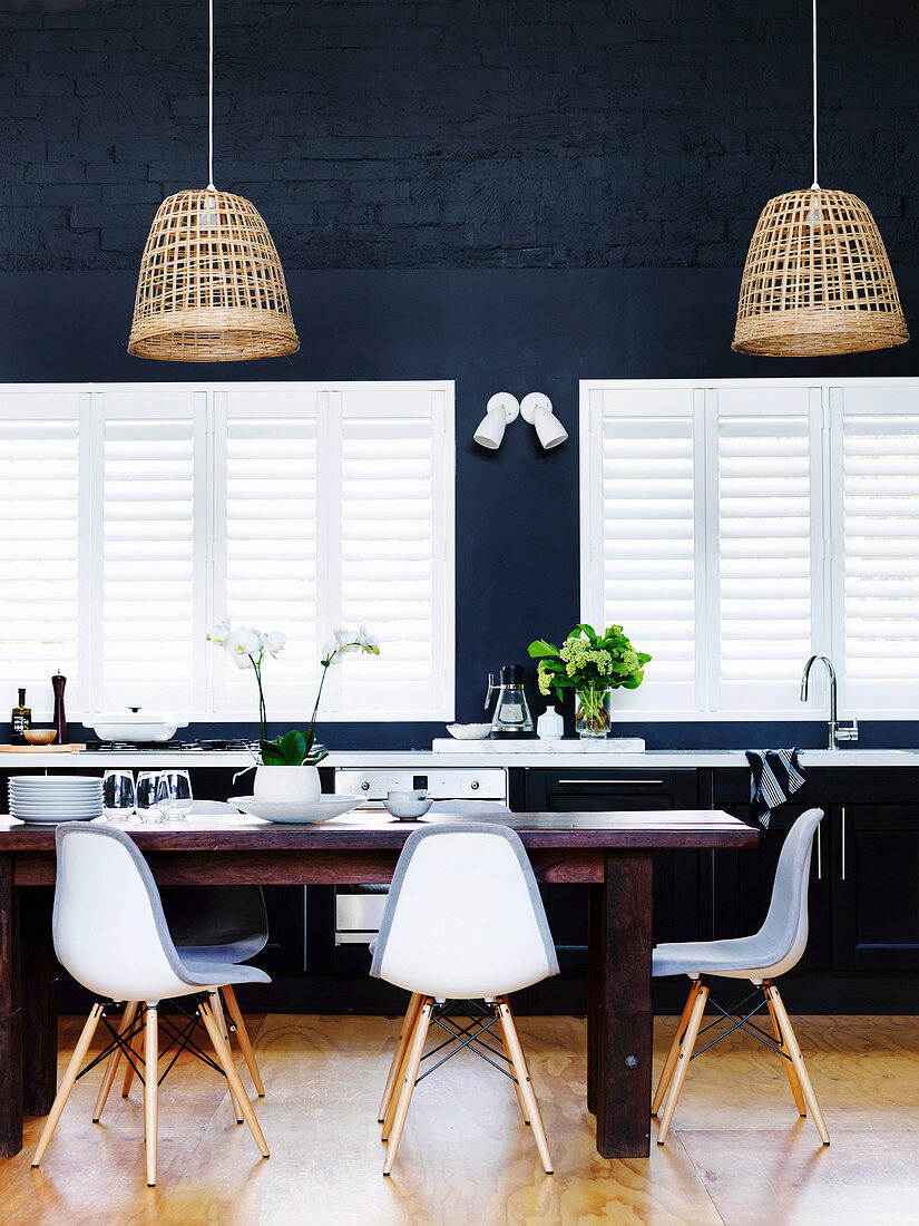 Esstisch mit Repliken von Klassikerstühlen for Fenstern und dunkelblauer Wand in offene Küche