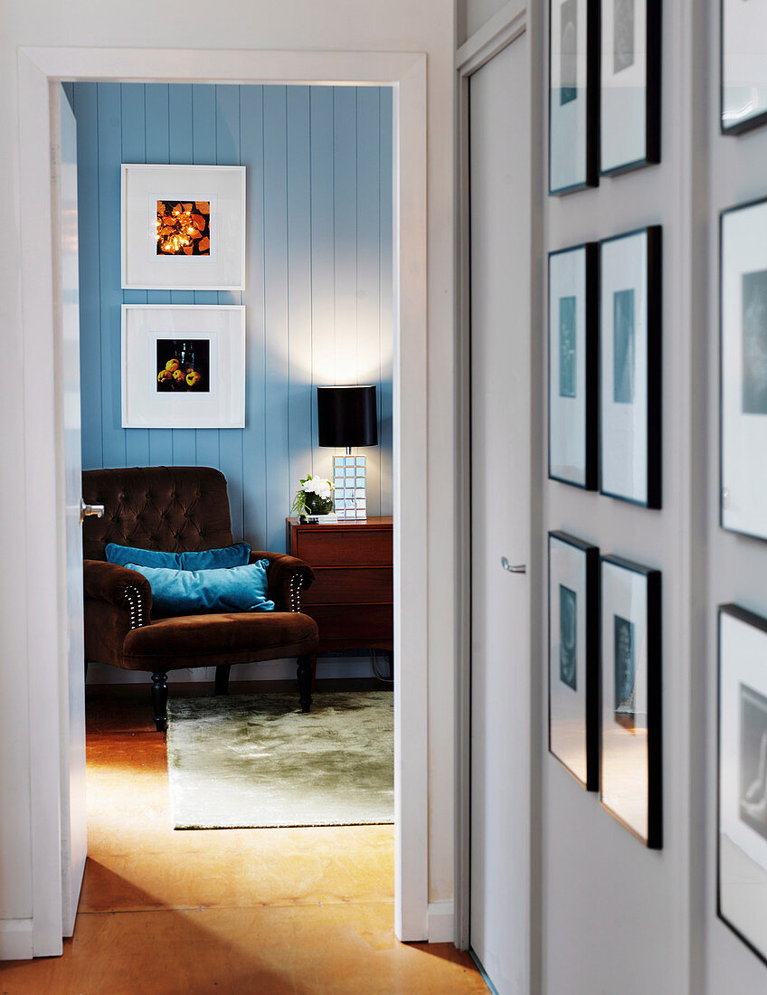 Hallway with framed photos and view of armchairs in the bedroom