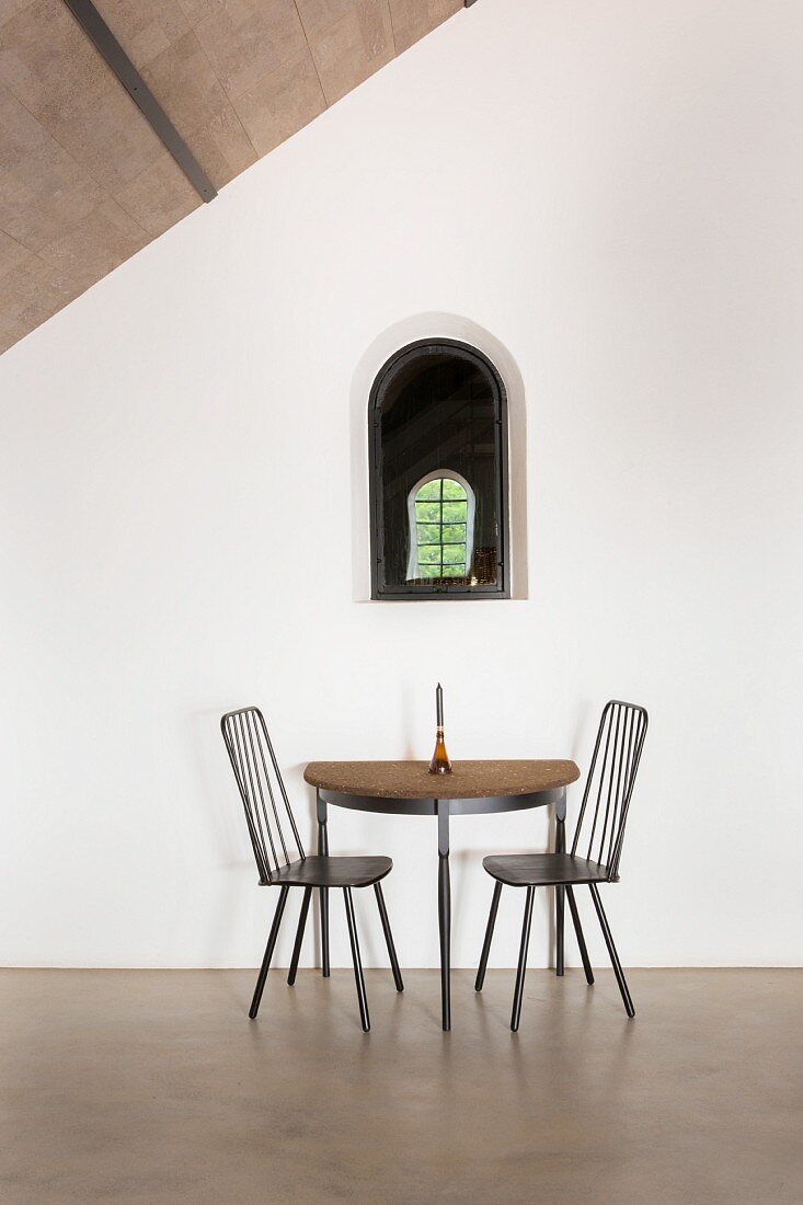 Halbrunder Tisch und zwei Stühle unter kleinem Bogenfenster