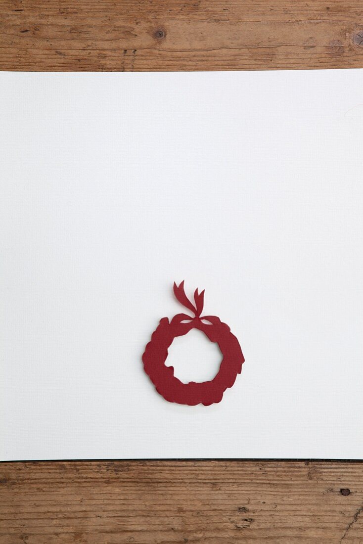 Christmas wreath cut out of red paper on white surface