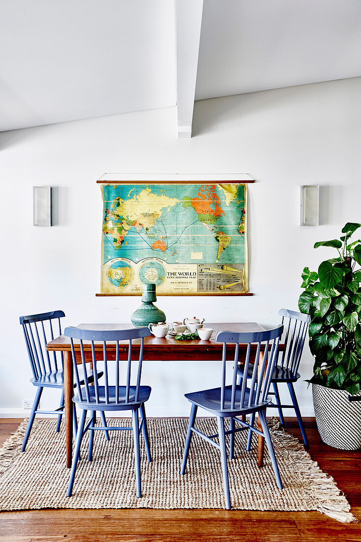 Blaue Windsorstühle um einen Holztisch vor einer alten Weltkarte
