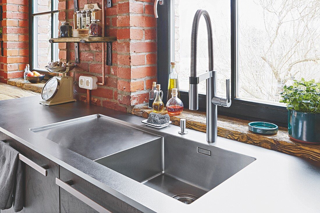A stainless steel sink in front of a window and a brick wall