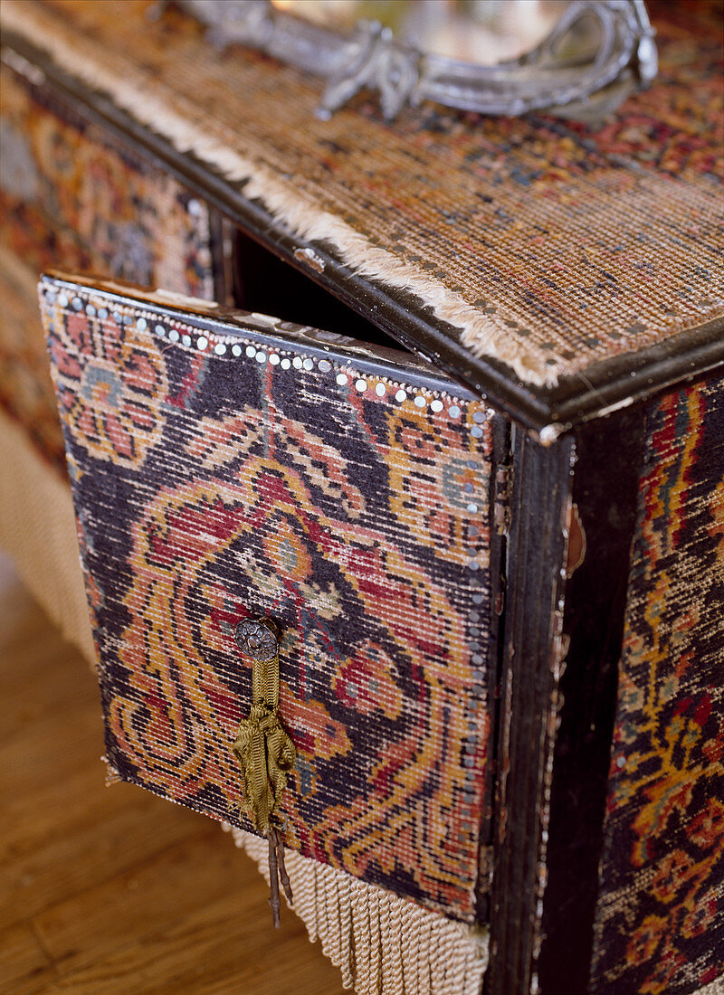 Detail einer schwarzen mit altem Teppich bezogenen Kommode