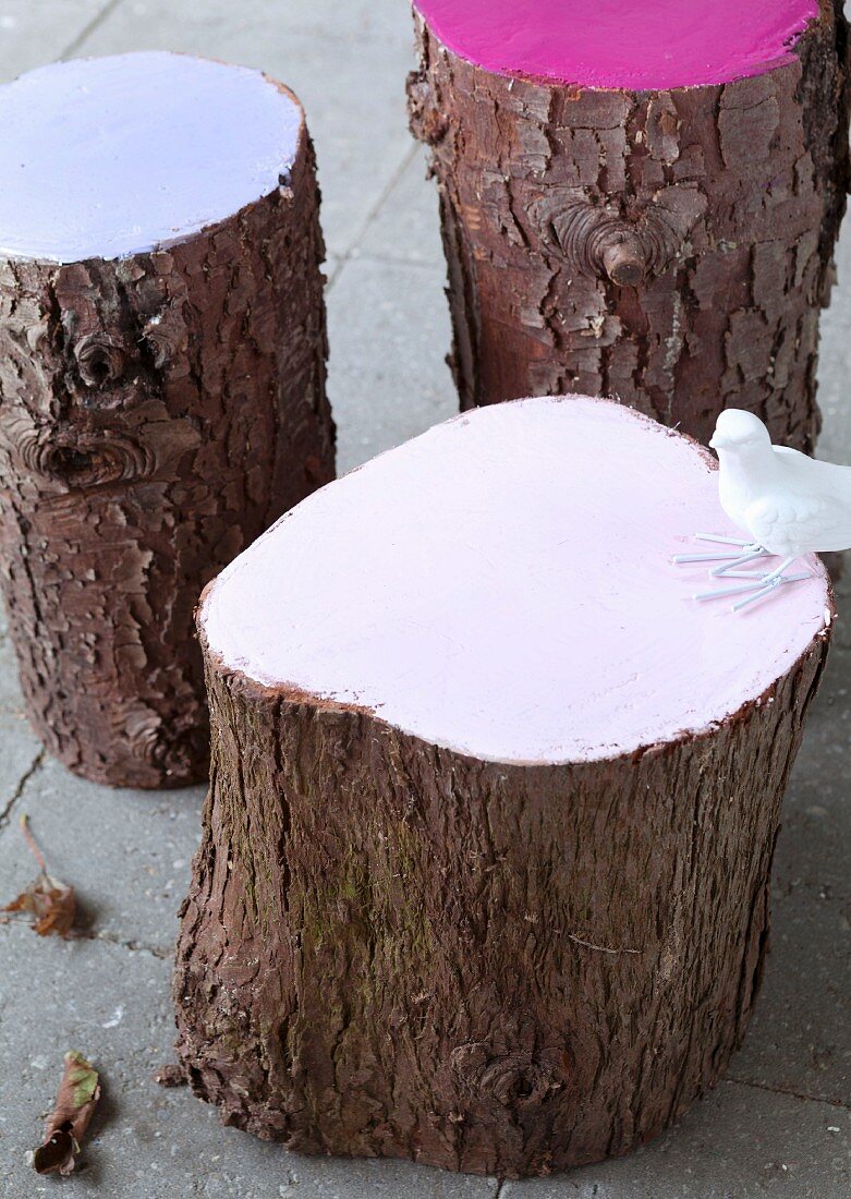 Baumstamm-Hocker mit pastellfarben lackierter Schnittfläche und weißer Vogelfigur